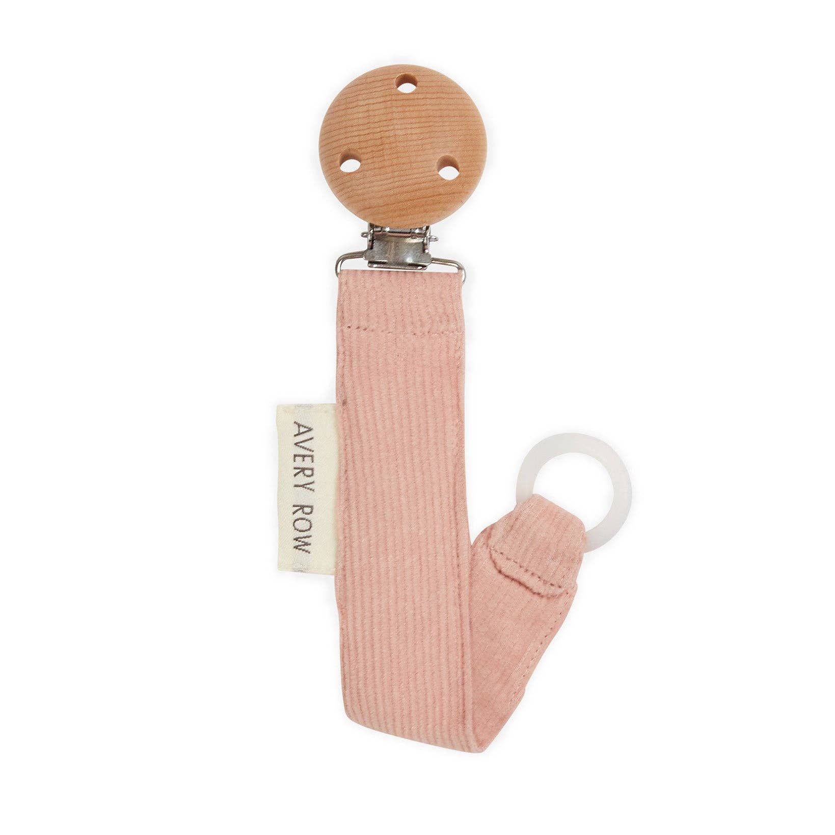 A blush pink corduroy pacifier clip with a round wooden clasp at the top and a soft fabric strap that loops into a silicone ring for attaching a pacifier. A small cream-colored label on the side reads “AVERY ROW” in simple lettering. The clip has a minimalist, elegant look, combining natural materials and gentle colors for a stylish and practical baby accessory.