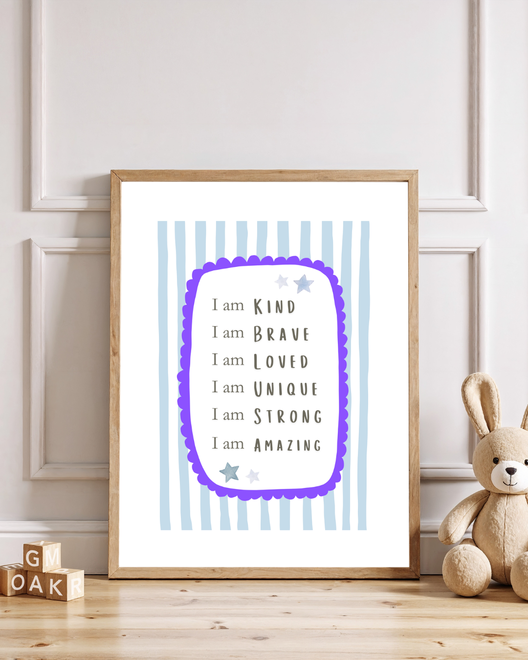 Nursery affirmation wall art print featuring positive “I am” statements in a wooden frame with blue striped background, styled in a neutral children’s room with teddy bear décor.