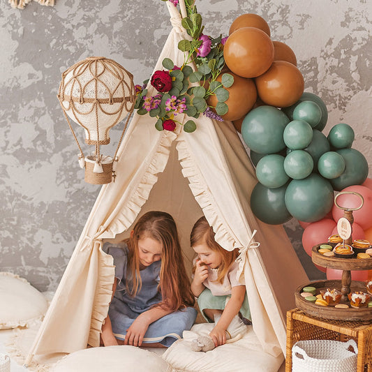 Two children inside a teepee with balloons and decorative items in the background.